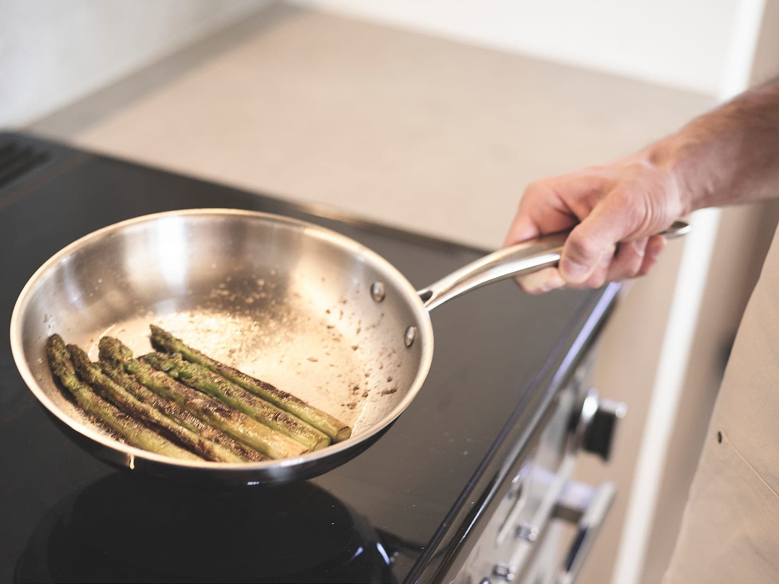 Asparagus cooking in an uncoated stainless steel skillet on the stovetop, seen from above