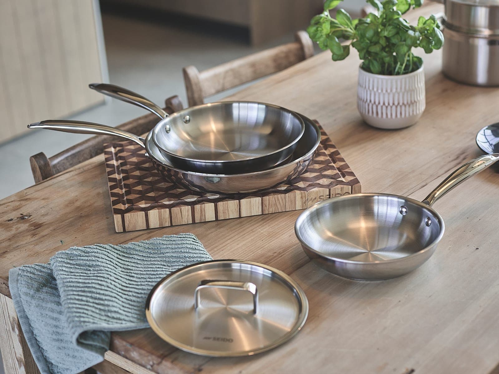 Three sizes of SEIDO stainless steel skillet on a wooden board