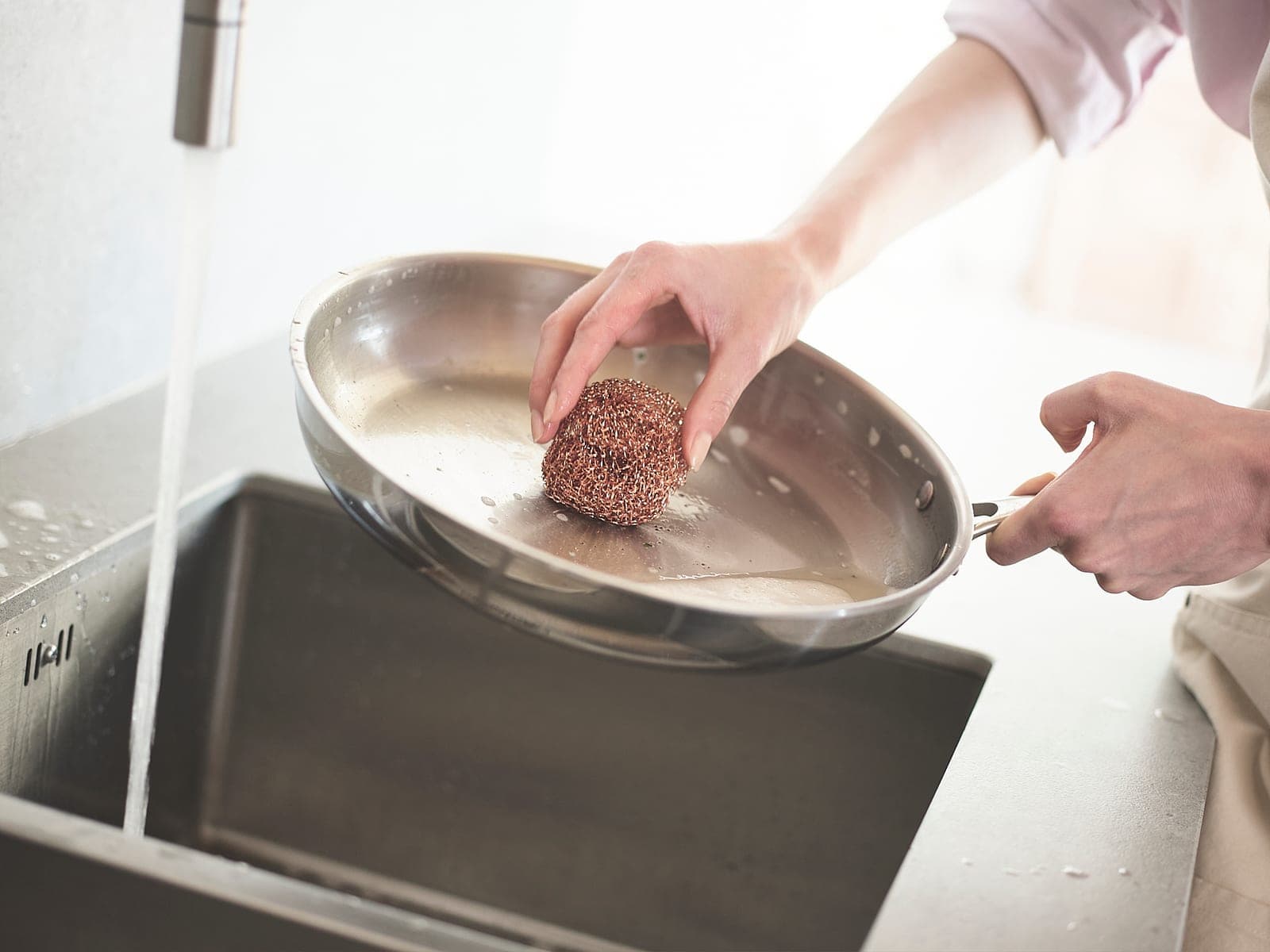 Washing a stainless steel skillet by hand under a running tap